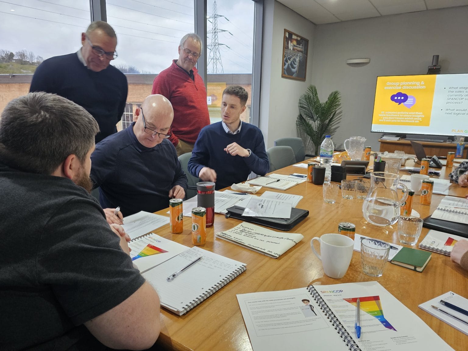 Senior managers reviewing workbooks together at a meeting table in a Plan Grow Do session