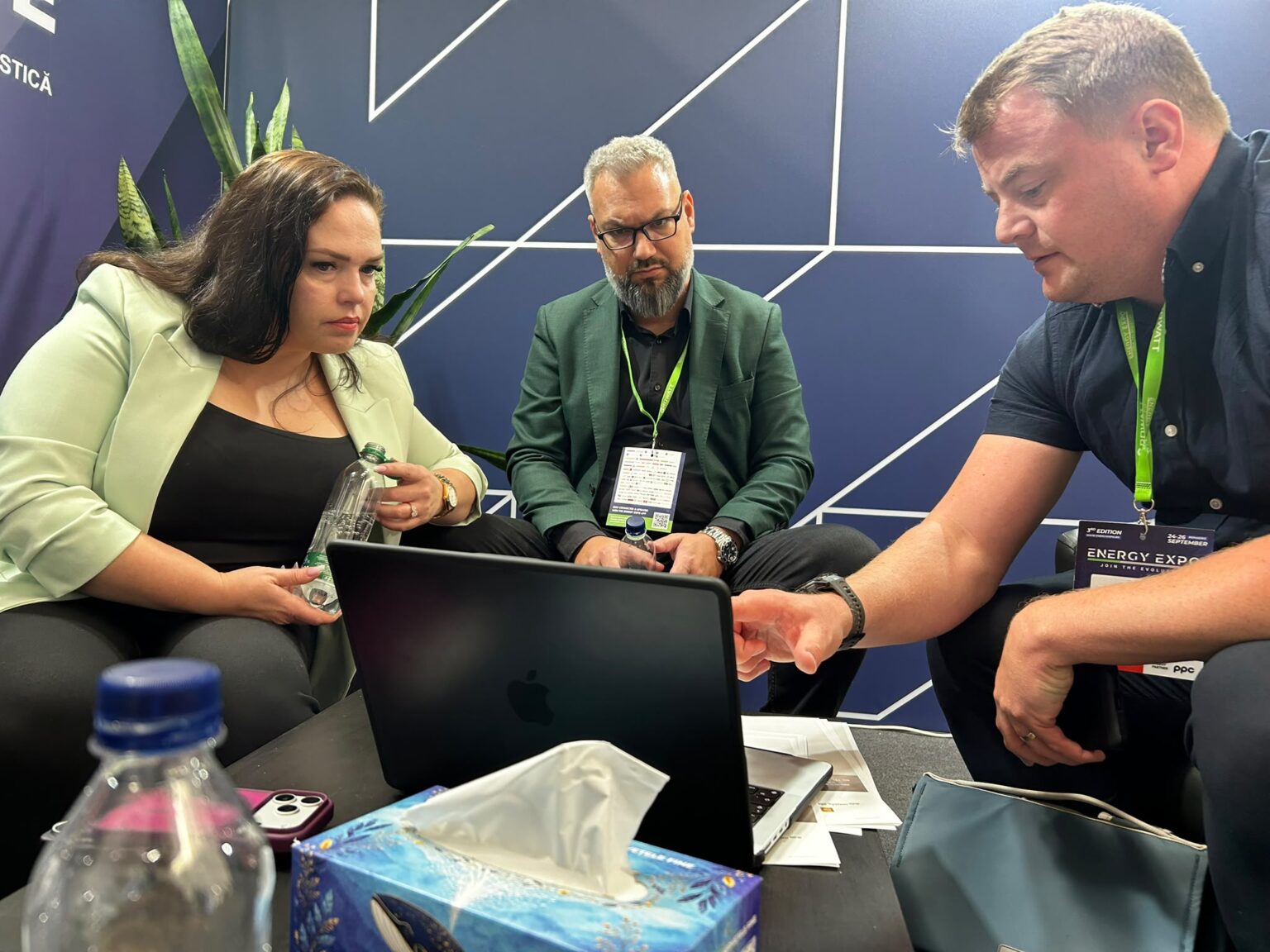 Three people around a laptop at an industry expo during a live demonstration